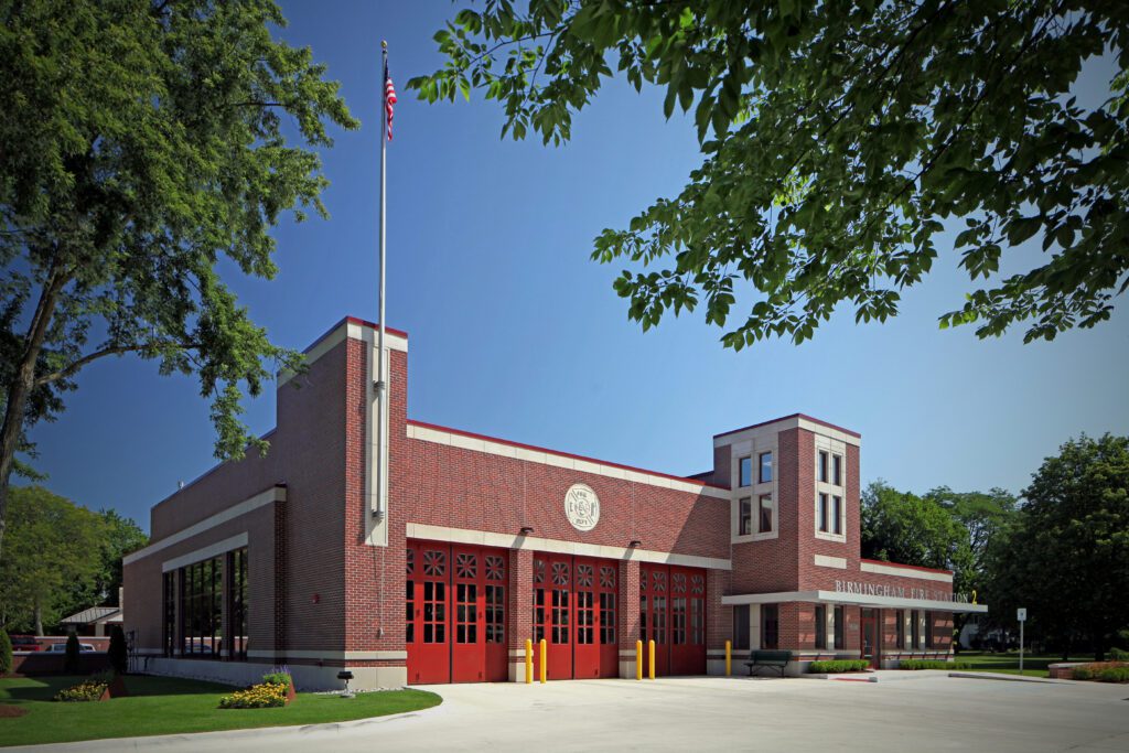 IMG_9935_edited-1 BJB copy Modern brick fire station with red doors and flagpole, surrounded by trees and landscaping, showcasing Sidock Group’s architectural design excellence in community infrastructure.
